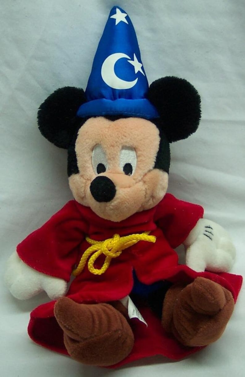 May include: A plush Mickey Mouse wearing a red robe with a yellow rope belt and a blue wizard hat with a white crescent moon and star.