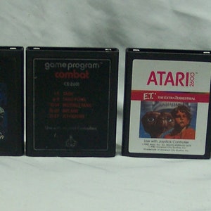 May include: A collection of eight vintage Atari game cartridges, including Pac-Man, Asteroids, Combat, E.T. the Extra-Terrestrial, Defender, and Missile Command. The cartridges are black with white text and graphics.