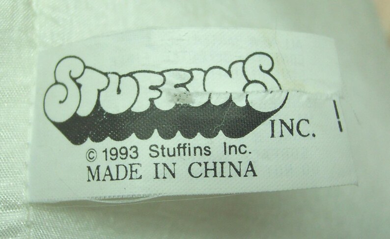 May include: A white fabric tag with the word "STUFFINS" in a black, bubble-style font. Below the logo are the words "INC." and "&copy; 1993 Stuffins Inc. MADE IN CHINA."