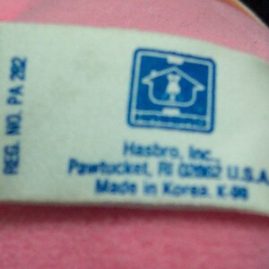 May include: White tag with blue text and a blue logo of a house with a person inside. The text reads "REG. NO. PA 282", "Hasbro, Inc.", "Pawtucket, RI 02862 U.S.A.", and "Made in Korea E. 98".
