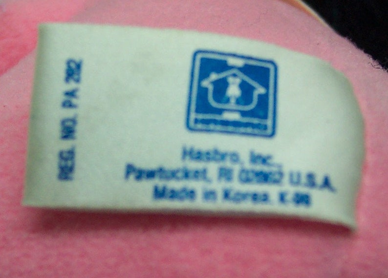 May include: White tag with blue text and a blue logo of a house with a person inside. The text reads "REG. NO. PA 282", "Hasbro, Inc.", "Pawtucket, RI 02862 U.S.A.", and "Made in Korea E. 98".