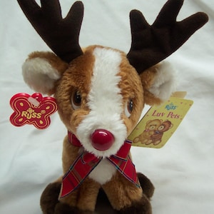 May include: A plush reindeer toy with brown fur, white accents, and a red nose. It has large brown antlers, a red plaid scarf, and a tag that reads "Russ Luv Pets."
