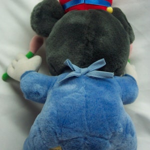 Puede incluir: Un juguete de peluche de Mickey Mouse vestido de director de orquesta. Lleva un sombrero rojo con una banda azul, un uniforme azul con una pajarita azul y sostiene una batuta de director.