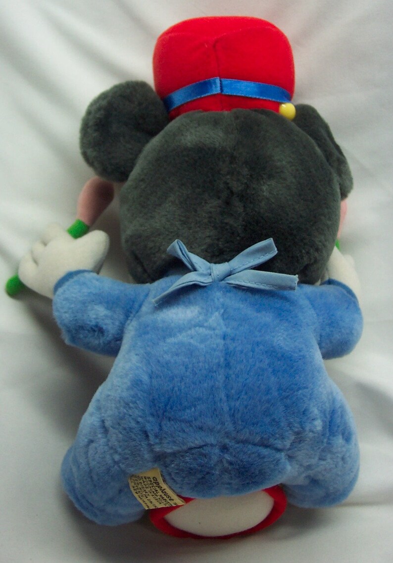 Puede incluir: Un juguete de peluche de Mickey Mouse vestido de director de orquesta. Lleva un sombrero rojo con una banda azul, un uniforme azul con una pajarita azul y sostiene una batuta de director.