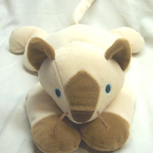 May include: A plush Siamese cat toy in cream and brown. The toy has brown ears, paws, and a face marking. It features blue eyes and thin, brown whiskers. The cat is lying down with its tail extended.