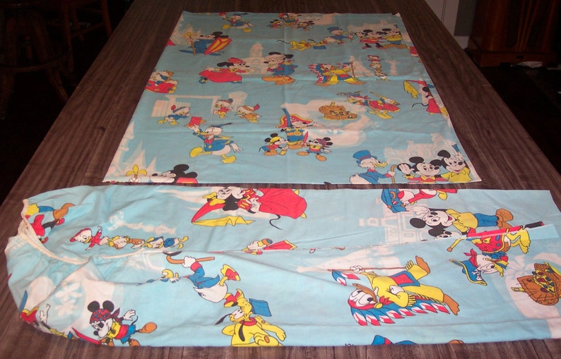 Puede incluir: Un juego de s&aacute;banas de cama doble de color azul y blanco con un estampado vintage de Disney con Mickey Mouse, Minnie Mouse, Donald Duck, Goofy y Pluto. Los personajes se representan en varias poses y escenarios, incluyendo un desfile, un castillo y un barco.