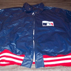 May include: A blue nylon jacket with white stripes on the sleeves and red and white stripes on the cuffs. The jacket has a zipper closure and a baseball logo on the front.
