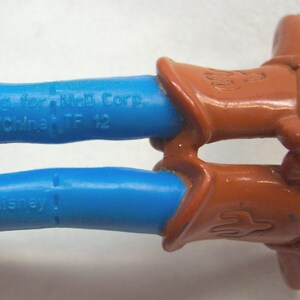 Pu&ograve; includere: Primo piano delle gambe di un giocattolo da cowboy in plastica blu con stivali marroni. L'iscrizione sulle gambe recita "Mfg for Mel Corp. China/China TF 12" e "&copy; Disney".