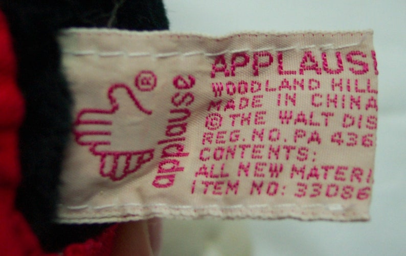 May include: Pink and white fabric tag with the text "Applause Woodland Hills Made in China &copy; The Walt Disney Reg. No. PA 436 Contents: All New Material Item No: 33086"