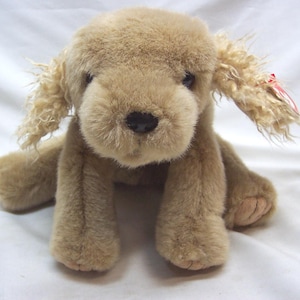 May include: A plush brown and white dog toy with floppy ears. The toy is sitting on a white surface.
