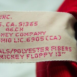 May include: A white tag with pink text that reads "INC. LS. CA. 91365 46.CH DISNEY COMPANY OHIO LIC. 6905 (CA) MATERIALS/POLYESTER FIBERS MICKEY FLOPPY 13"