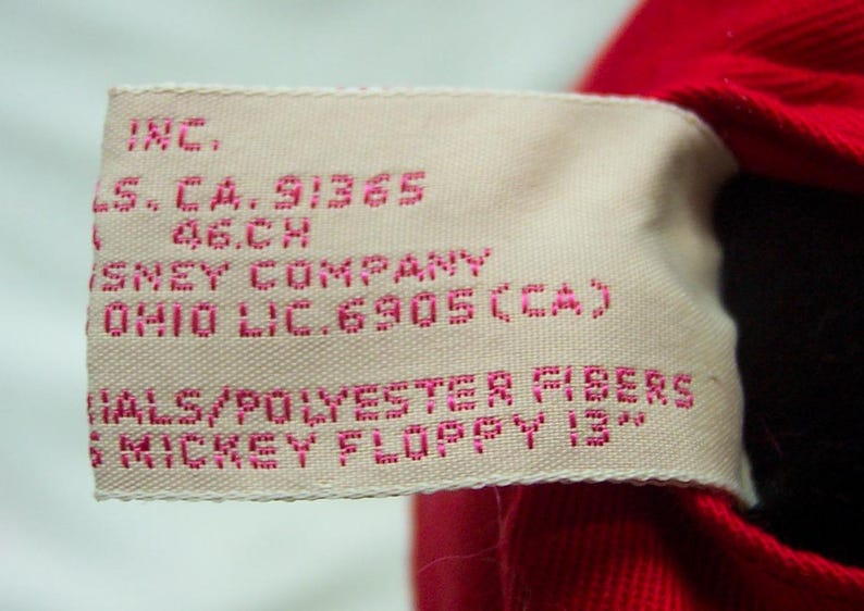 May include: A white tag with pink text that reads "INC. LS. CA. 91365 46.CH DISNEY COMPANY OHIO LIC. 6905 (CA) MATERIALS/POLYESTER FIBERS MICKEY FLOPPY 13"