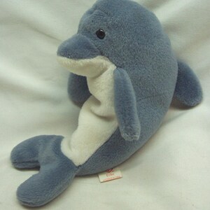 May include: A plush dolphin toy in shades of blue and white. The stuffed animal has a rounded body, flippers, and a tail. The dolphin has a white belly and a tag that reads "Echo".