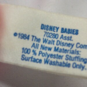 May include: A white tag with blue text that reads "DISNEY BABIES 70280 Asst. &copy;1984 The Walt Disney Company All New Materials: 100% Polyester Stuffing. Surface Washable Only."