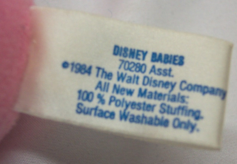 May include: A white tag with blue text that reads "DISNEY BABIES 70280 Asst. &copy;1984 The Walt Disney Company All New Materials: 100% Polyester Stuffing. Surface Washable Only."