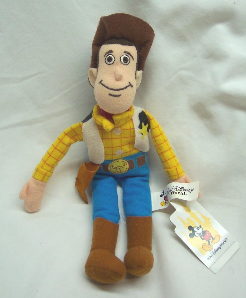 May include: A plush toy of Woody from Toy Story, wearing a brown cowboy hat, yellow plaid shirt, blue jeans, and brown boots. The toy has a white vest and a sheriff's badge. A Disney World tag is attached.