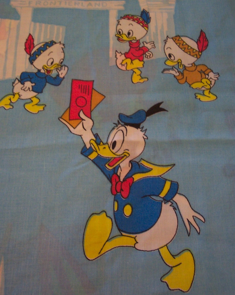 Puede incluir: Una ilustraci&oacute;n vintage de Donald Duck con un traje de marinero y sosteniendo un mapa rojo y blanco. Otros tres patos llevan tocados de nativos americanos y est&aacute;n en el fondo. El fondo es azul con un borde blanco.