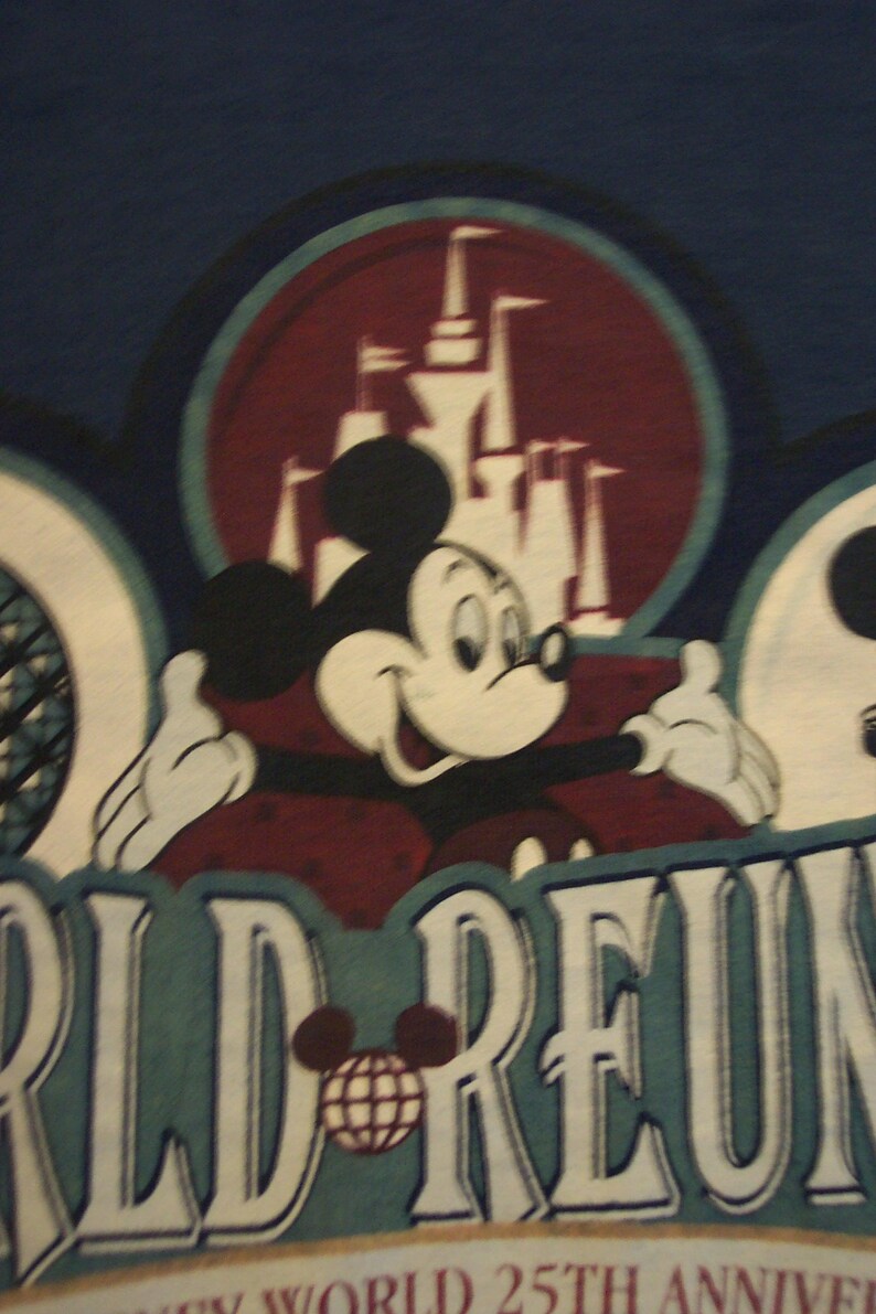 May include: A dark blue t-shirt featuring a graphic of Mickey Mouse with arms outstretched in front of a castle silhouette. The text reads WORLD REUNION and WALT DISNEY WORLD 25TH ANNIVERSARY, with a small globe icon replacing the letter O.