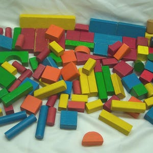 May include: A large collection of wooden building blocks in various geometric shapes including cubes, rectangular prisms, cylinders, and semi-circles. The blocks are painted in bright primary and secondary colors such as red, blue, yellow, green, and orange.