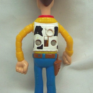 Pu&ograve; includere: Una figurina di plastica di Woody del franchise Toy Story. Woody indossa un cappello da cowboy marrone, una camicia gialla con un bordo rosso, un gilet bianco con un motivo di mucca bianco e nero, jeans blu e stivali da cowboy marroni.