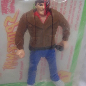Pu&ograve; includere: Una action figure di plastica di un uomo che indossa una giacca di pelle marrone, jeans blu e una maschera rossa e nera. La figura &egrave; confezionata in un sacchetto di plastica trasparente con uno sfondo verde e giallo. Il sacchetto ha le parole "Spider-Man" e "comics" stampate su di esso.