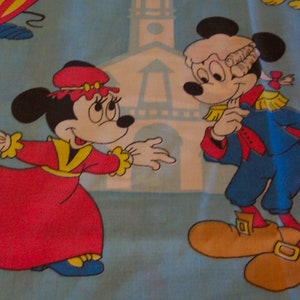 Puede incluir: Una tela vintage con Mickey y Minnie Mouse vestidos con atuendos coloniales. Mickey lleva un uniforme azul y rojo con una peluca blanca y ribetes dorados. Minnie lleva un vestido rojo con una faja amarilla y un sombrero rojo. El fondo es azul claro con un edificio blanco.