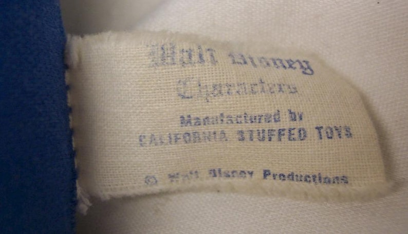 K&ouml;nnte beinhalten: Ein wei&szlig;es Stoff-Etikett mit blauem Text, der "Walt Disney Characters Manufactured by California Stuffed Toys &copy; Walt Disney Productions" lautet.