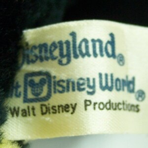 Peut inclure: Une &eacute;tiquette blanche avec du texte bleu qui dit "Disneyland", "Walt Disney World" et "Walt Disney Productions". L'&eacute;tiquette a un petit logo de t&ecirc;te de Mickey Mouse au centre.