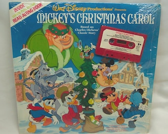 May include: A Walt Disney Productions Mickey's Christmas Carol read-along book and cassette tape set. The cover features Mickey Mouse, Donald Duck, Goofy, and Scrooge McDuck in a snowy village scene with a Christmas tree. A red cassette tape is attached to the front.