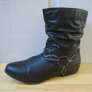 May include: Black leather ankle boots with a gold chain ankle bracelet. The boots have a pointed toe and a low heel.