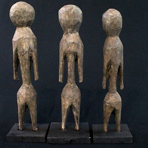 以下が含まれることがあります： 丸い頭とスタイリッシュな手足を持ち、人間の姿をした木製の彫刻が3つあります。彫刻は黒い台座の上に立っており、一列に並んでいます。