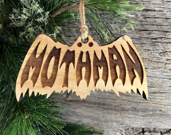 May include: Wooden Christmas ornament shaped like a bat with the word "Mothman" carved into it.