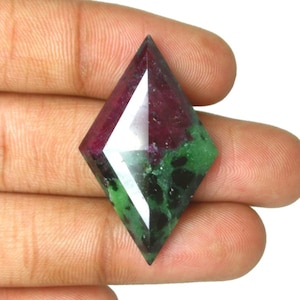 Puede incluir: Una piedra preciosa de rubí zoisita tallada en forma de diamante, con una clara división de color entre el rojo magenta intenso y el verde bosque moteado con inclusiones negras, pulida con una superficie lisa y reflectante.