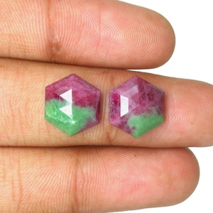Peut inclure: Deux pierres précieuses hexagonales à facettes présentant une séparation de couleurs distincte entre le rose magenta vif et le vert forêt profond. Ces pierres présentent une surface supérieure plate avec des facettes géométriques.