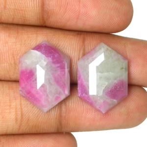 May include: Two loose hexagonal gemstones featuring a faceted surface with a mix of opaque white and vibrant magenta pink coloration. These stones display a geometric six-sided shape with polished edges and a flat top, showcasing natural color variations.