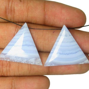 Può includere: Due pietre preziose di agata blu a forma triangolare con superficie sfaccettata e motivi a bande azzurre e bianche. Le pietre presentano un piccolo foro nella parte superiore e sono infilate su un sottile filo nero.