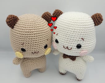 Può includere: Due animali di peluche all'uncinetto, uno marrone e uno bianco, con facce ricamate e cuori intorno a loro.