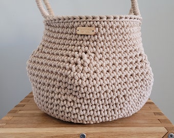 May include: A beige crocheted storage basket with two handles. The basket has a wooden tag that says "Handmade for you".