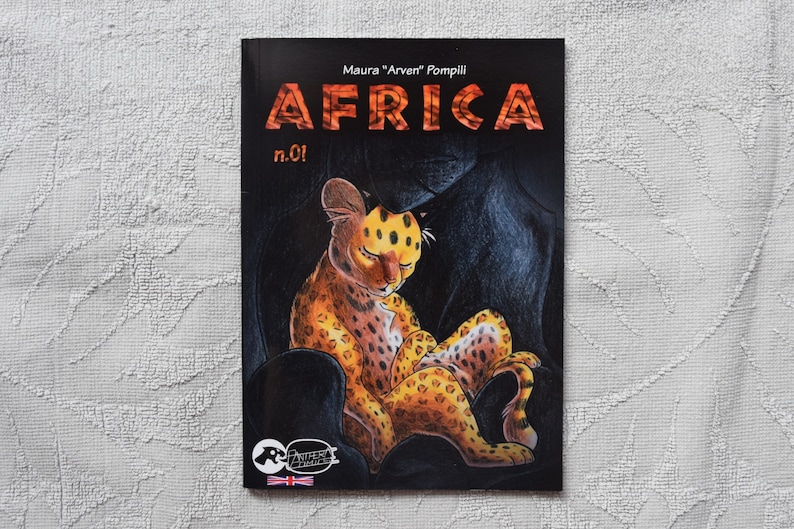 Pode incluir: Uma capa de banda desenhada com fundo preto que apresenta um filhote de guepardo amarelo e laranja enroscado numa caverna escura. O t&iacute;tulo "AFRICA" est&aacute; escrito em letras vermelhas com contorno branco. O texto "Maura "Arvent" Pompili" e "n.01!" tamb&eacute;m s&atilde;o vis&iacute;veis na capa.