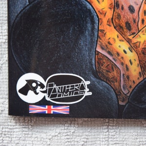Pode incluir: Um adesivo preto e branco com o texto "Panthera Comics" e uma imagem estilizada de uma cabe&ccedil;a de pantera. O adesivo est&aacute; em um fundo preto com uma estampa de animal amarelo e marrom.