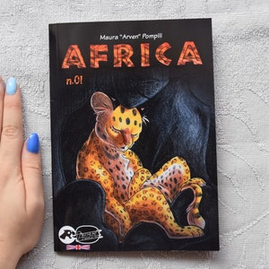 Pode incluir: Uma capa de banda desenhada com fundo preto que apresenta um filhote de guepardo manchado de amarelo e laranja dormindo sobre uma pantera negra. O t&iacute;tulo da banda desenhada &eacute; "AFRICA" com o n&uacute;mero "n.01" abaixo. O nome do autor &eacute; "Maura "Arven" Pompili" acima do t&iacute;tulo.