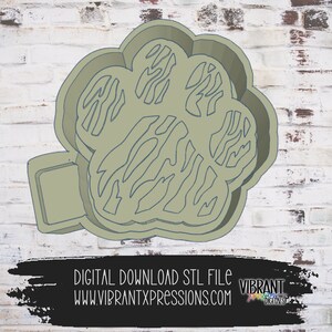 May include: A 3D printed paw print cookie cutter with a striped design. The cutter is light green and has a small rectangular base.