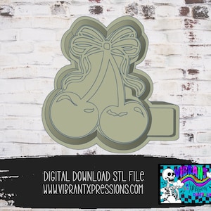 May include: A 3D printed STL file design for a cookie cutter shaped like two cherries with a bow on top. The design is in a light brown color.