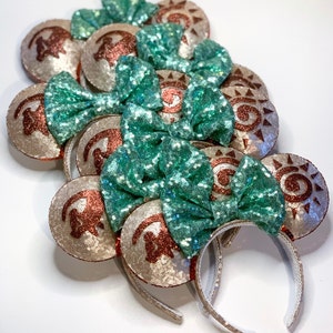 May include: A set of six gold and teal Minnie Mouse ears with a sun design. The ears are made of sequins and have a bow on top.