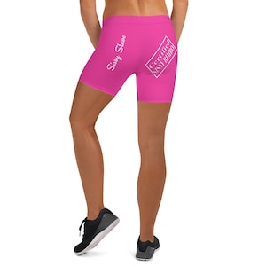 May include: Bright pink biker shorts with white text that reads "Sissy Slave" and "Certified Sissy Bimbo". The shorts are form-fitting and made of a stretchy material. The shorts are worn by a person.