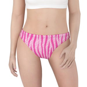 May include: Pink and white striped underwear. The underwear has a low-rise waist and a brief cut. The stripes are vertical and wavy, creating a zebra-like pattern. The background is white.