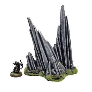 Könnte beinhalten: Ein graues, zerklüftetes, felsiges Geländemodell mit grünem Sockel. Das Modell ist aus Kunststoff und für Tabletop-Spiele konzipiert.