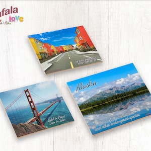 May include: Three square coasters with different images and text. The first coaster features a colorful street scene with the text "If you dream, you can do it". The second coaster features a view of the Golden Gate Bridge with the text "Gold in Peace, Iron in War". The third coaster features a mountain lake scene with the text "Alaska, Land of the individual and other endangered species".