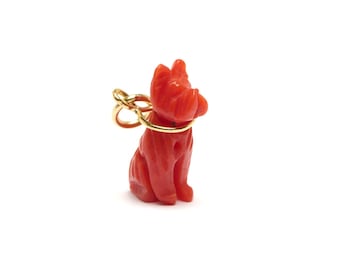 May include: A red coral dog charm with a gold chain. The dog is sitting with its head tilted up.