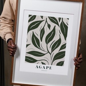 May include: A framed print with a white background and a green leaf pattern. The print has the word "AGAPE" in dark green text and the words "John 13:34" in smaller dark green text.
